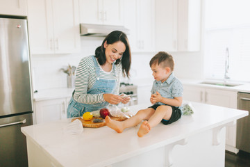 A mother and son preparing food together in a white kitchen.