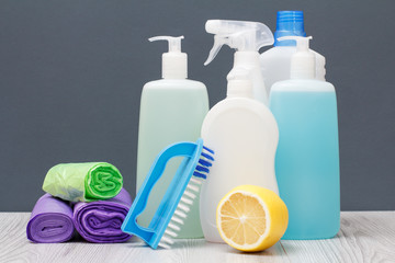 Bottles of dishwashing liquid, brush and lemon on gray background.