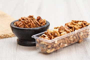 Walnuts in stone bowl and plastic container on a wooden background.