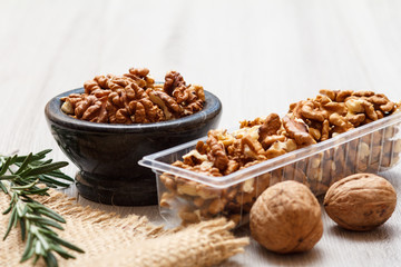 Walnuts in stone bowl and plastic container on a wooden background.