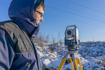 A surveyor conducts a topographical survey for the cadastre at a construction site in winter
