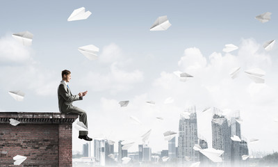 Businessman or student on roof edge making calls and cityscape at background