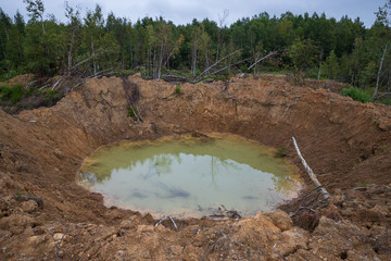 Hole on ground from powerful explosion. Bomb crater in the forest. Disposal of explosives.