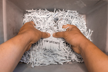 Cutted pieces of paper in a shredder basket. The hands hold the shreddered lines of paper that form...