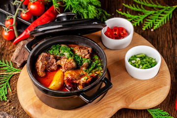 The concept of Serbian cuisine. Juicy baked beef in its own juice with potatoes, vegetables and greens. Serve in an iron fire on a wooden board.