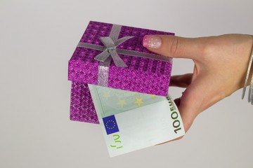 A woman with a manicure holding a gift box full of euro banknotes.Rolled banknotes wrapped in a...