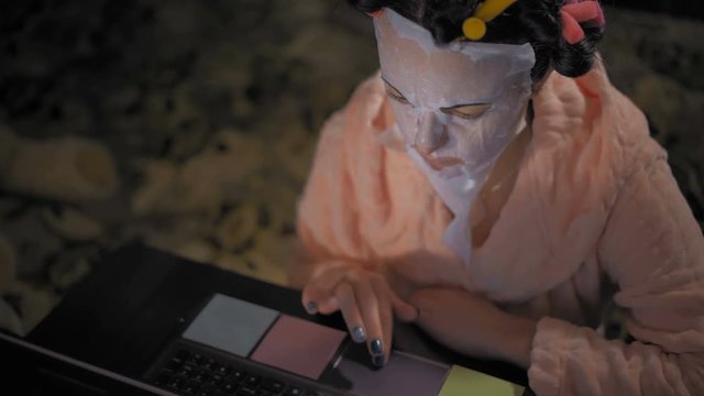 Close-up, Woman in Pink Robe Works on Laptop in Rejuvenating Mask