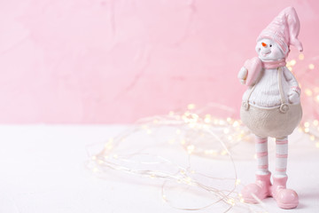Little decorative snowman  toy and fairy lights on bright  pink wooden  background.