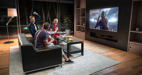 Group of fans are watching a soccer moment on the TV and celebrating a goal, sitting on the couch in the living room.