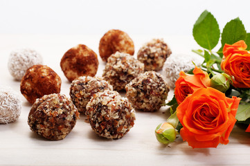 Useful fitness sweets from dried fruits, nuts and seeds, no sugar on a white background. Near orange roses. Shallow depth of field, blurred background. Macro shooting
