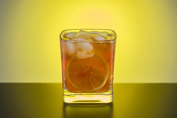 Transparent glass of whiskey with lemon and ice, close-up on the background of the light source