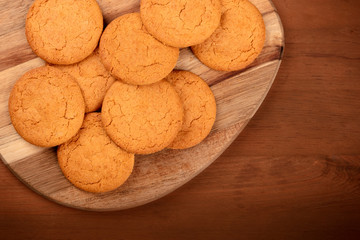 A closeup photo of ginger biscuits on a wooden tray, shot from above on a dark rustic background with copy space