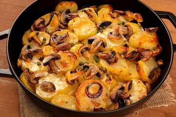 A closeup photo of a braiser with cooked vegetables, potatoes, green peas, mushrooms on a dark rustic wooden background, a vegan dinner