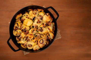 A photo of a dutch oven with cooked vegetables, potatoes, green peas, white mushrooms, shot from above on a dark rustic wooden background with a place for text, a vegan meal