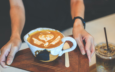 Women holding a hot white cup of coffee latte in hands on wood table in coffee shop.
