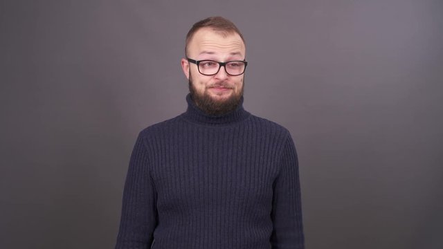 Portrait of tired yawning man with beard and glasses, dressed in a turtleneck. Isolated on grey background.