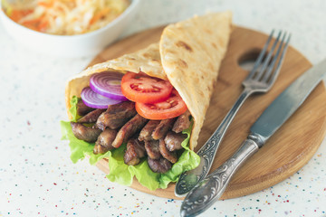 Handmade doner kebab is lying on the white table made of artificial stone Shawarma on the wooden cutting board with chicken meat, onions, salad lies on a dark old wooden table.