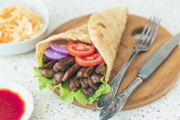 Handmade doner kebab is lying on the white table made of artificial stone Shawarma on the wooden cutting board with chicken meat, onions, salad lies on a dark old wooden table.