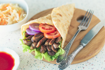 Handmade doner kebab is lying on the white table made of artificial stone Shawarma on the wooden cutting board with chicken meat, onions, salad lies on a dark old wooden table.