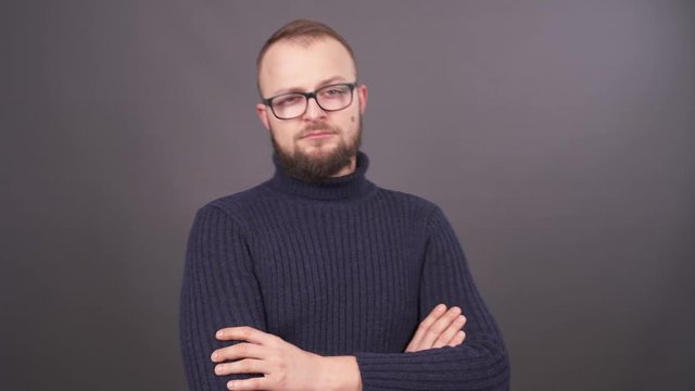 Portrait of a bearded young man in glasses demonstrating contempt. Isolated on grey background.
