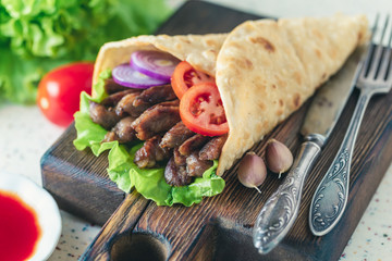 Handmade doner kebab is lying on the white table made of artificial stone Shawarma on the wooden cutting board with chicken meat, onions, salad lies on a dark old wooden table.