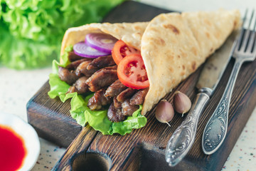 Handmade doner kebab is lying on the white table made of artificial stone Shawarma on the wooden cutting board with chicken meat, onions, salad lies on a dark old wooden table.