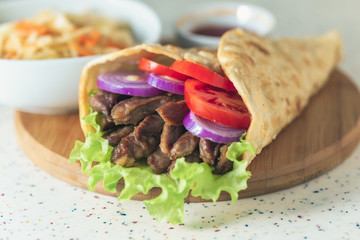 Handmade doner kebab is lying on the white table made of artificial stone Shawarma on the wooden cutting board with chicken meat, onions, salad lies on a dark old wooden table.