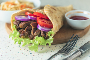 Handmade doner kebab is lying on the white table made of artificial stone Shawarma on the wooden...