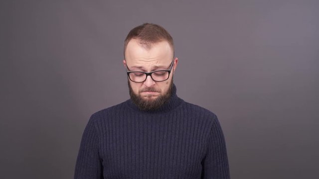 Portrait of a young bearded man in glasses, who asking for forgiveness. Feeling confused. Isolated on grey background.