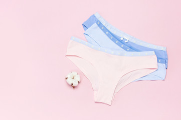 Female pastel cotton set panties and cotton flower on pink background top view flat lay with copy space for text. Fashion blog, Colorful women's natural underwear, advertising, shopping concept.