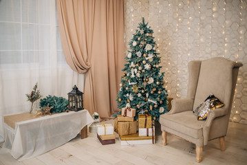 Stylish, calm festive, Christmas interior with a Christmas tree, gifts, an armchair. Beige and gold in the interior