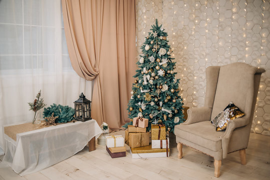 Stylish, calm festive, Christmas interior with a Christmas tree, gifts, an armchair. Beige and gold in the interior