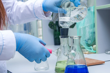 Fototapeta premium a chemist holds a glass test tube in his hand, overflows a liquid solution, conducts an analysis reaction using various reagent options using chemical production.