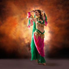 Gorgeous woman bellydancer dancing in traditional bellydance costume over colored studio background.