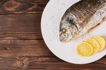 Baked dorada fish on a white plate on wooden background.