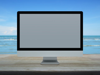 Desktop modern computer monitor with white wide screen on wooden table over tropical sea and blue sky with white clouds