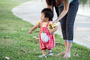 baby walking in green park holding hands of mother