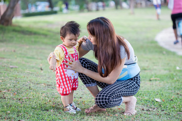 baby walking in green park holding hands of mother