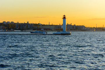 A lighthouse in the sea at the entrance to the port against the backdrop of a beautiful evening blue sky in soft colors. Summer seascape. White lighthouse with a red top. Black Sea. Seaport of Odessa