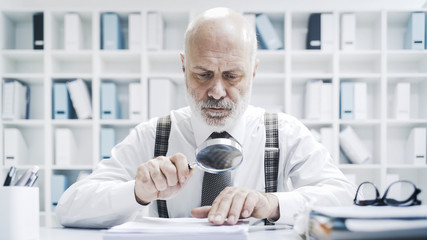 Corporate businessman checking paperwork with a magnifier