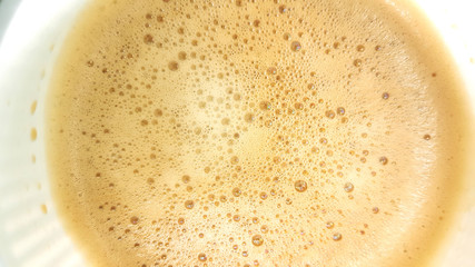 Bubbles of hot coffee close up in white glass.