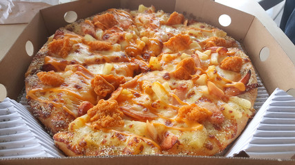 Slice a large of pizza in a crisp delivery box with cheesy chicken and pineapple for a quick meal.