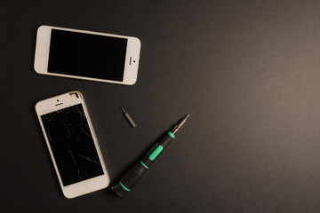 Broken white phone with repair tools kit on the dark background	