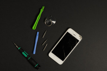Broken white phone with repair tools kit on the dark background	