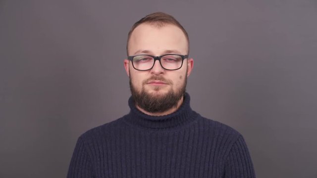 Portrait of a young bearded sleepy man in glasses that could hardly keep his eyes open. Isolated on a grey background.