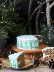 Celebratory cake decorated with painted Christmas trees on a dark background of branches and cones. Rustic style.