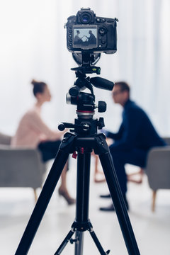 side view of businessman giving interview to journalist in office, camera on tripod on foreground
