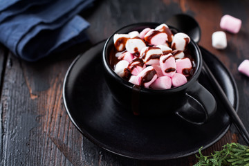 Hot chocolate with marshmallow candies in black ceramic cup on old dark vintage wooden background. Selective focus.