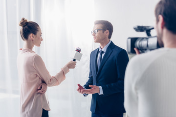 handsome businessman in glasses giving video interview to beautiful journalist in office
