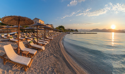 Sunbeds and umbrella on the beach at sunset time on Corfu Island, Greece